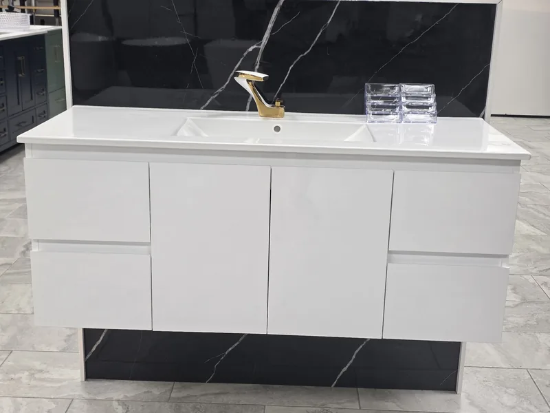 White floating vanity with a gold faucet against a black marble-look wall